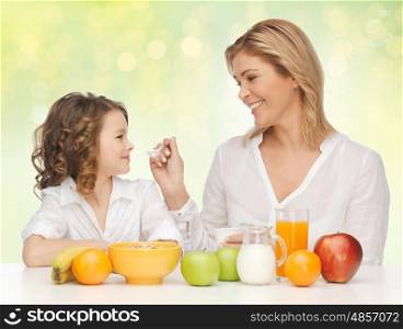 healthy eating, people, family and food concept - happy mother and daughter having breakfast over green holidays lights background