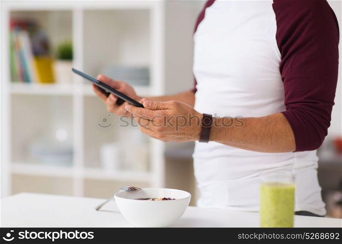 healthy eating, people, technology and diet concept - man with tablet pc computer having breakfast at home kitchen. man with tablet pc having breakfast at home