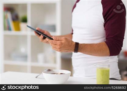 healthy eating, people, technology and diet concept - man with tablet pc computer having breakfast at home kitchen. man with tablet pc having breakfast at home