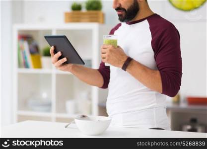 healthy eating, people, technology and diet concept - man with tablet pc computer and smoothie having breakfast at home kitchen. man with tablet pc having breakfast at home