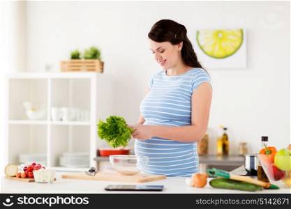 healthy eating, pregnancy and people concept - happy smiling pregnant woman with lettuce cooking vegetable salad at home kitchen. pregnant woman cooking vegetable salad at home