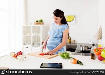 healthy eating, pregnancy and people concept - pregnant woman cooking and chopping cherry tomatoes at home kitchen. pregnant woman cooking vegetables at home