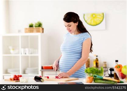 healthy eating, pregnancy and people concept - pregnant woman cooking and chopping vegetable at home kitchen. pregnant woman cooking vegetables at home