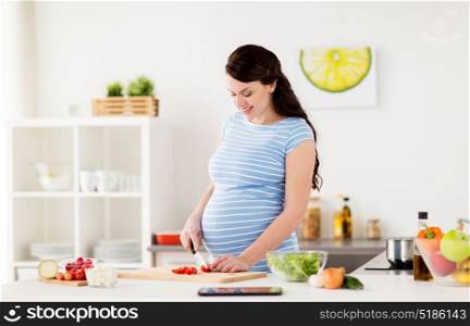 healthy eating, pregnancy and people concept - pregnant woman cooking vegetable salad and chopping cherry tomatoes at home kitchen. pregnant woman cooking vegetables at home