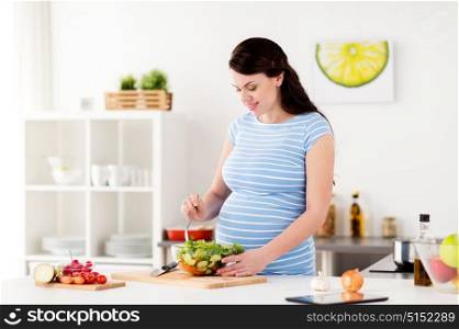 healthy eating, pregnancy and people concept - pregnant woman cooking vegetable salad at home kitchen. pregnant woman cooking vegetable salad at home