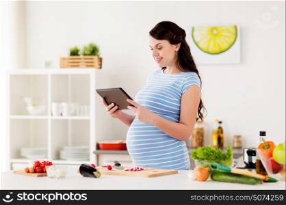 healthy eating, pregnancy and people concept - pregnant woman with tablet pc computer cooking vegetable salad at home kitchen. pregnant woman with tablet pc cooking at home