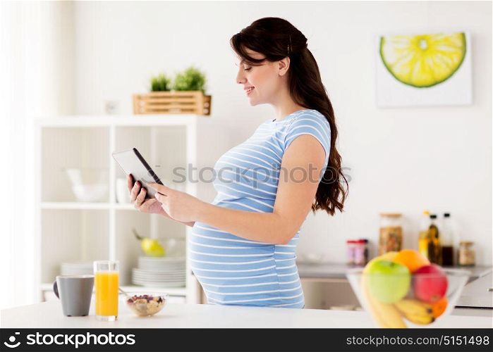 healthy eating, pregnancy and people concept - pregnant woman with tablet pc computer having breakfast at home kitchen. pregnant woman with tablet pc eating at home