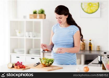healthy eating, pregnancy, food and people concept - pregnant woman cooking vegetable salad with feta cheese at home kitchen. pregnant woman cooking vegetable salad at home
