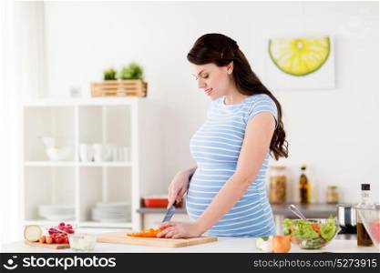 healthy eating, pregnancy, food and people concept - pregnant woman cooking vegetable salad and chopping pepper at home kitchen. pregnant woman cooking vegetable salad at home