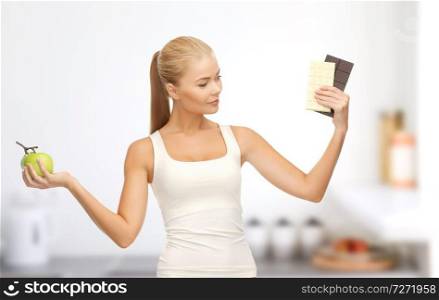 healthy eating, slimming and diet concept - happy woman choosing between green apple and chocolate over home kitchen room background. woman choosing between green apple chocolate