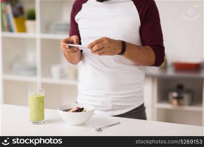 healthy eating, technology and people concept - man with smartphone having breakfast at home kitchen. man with smartphone having breakfast at home