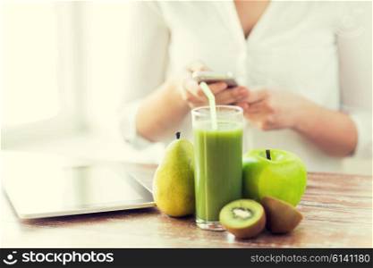healthy eating, technology, diet and people concept - close up of woman hands holding smartphone with tablet pc, fruits and fresh juice sitting at table