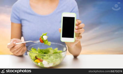healthy eating, technology, food and people concept - close up of young woman with smartphone and vegetable salad over sky background. close up of woman with smartphone eating salad. close up of woman with smartphone eating salad