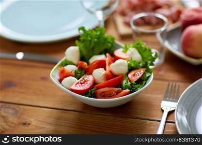 healthy eating, vegetarian food and culinary concept - bowl of vegetable salad with tomatoes and mozzarella cheese on wooden table. vegetable salad with mozzarella on wooden table
