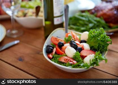 healthy eating, vegetarian food and culinary concept - bowl of vegetable salad with tomatoes, olives and mozzarella cheese on wooden table. vegetable salad with mozzarella on wooden table