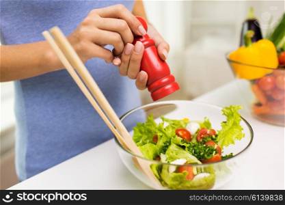 healthy eating, vegetarian food, cooking and people concept - close up of young woman seasoning vegetable salad with salt or pepper at home
