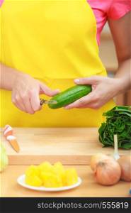 Healthy eating, vegetarian food, cooking, dieting and people concept. Closeup female hands in kitchen preparing fresh vegetables salad peeling cucumber