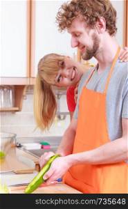 Healthy eating, vegetarian food, cooking, dieting and people concept. Loving young couple in kitchen preparing fresh vegetables salad peeling cucumber