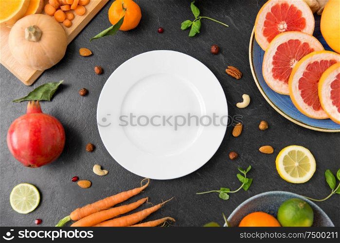 healthy eating, vegetarian food, diet and culinary concept - empty white plate and different vegetables and fruits on on slate table. plate, vegetables and fruits on on slate table