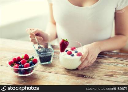 healthy eating, vegetarian food, diet and people concept - close up of woman hands with yogurt, berries and poppy or chia seeds on spoon