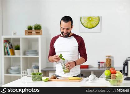 healthy eating, vegetarian food, diet and people concept - happy young man with blender cup and fruits cooking at home kitchen. man with blender cup cooking food at home kitchen