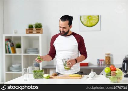 healthy eating, vegetarian food, diet and people concept - happy young man with blender cup and fruits cooking at home kitchen. man with blender cup cooking food at home kitchen