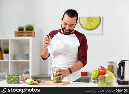 healthy eating, vegetarian food, diet and people concept - happy young man with blender and fruits cooking at home kitchen. man with blender cooking food at home kitchen