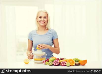 healthy eating, vegetarian food, diet, detox and people concept - smiling woman with squeezer squeezing fruit juice at home