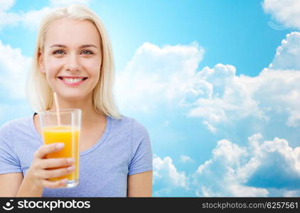 healthy eating, vegetarian food, diet, detox and people concept - smiling woman drinking orange juice or shake from glass over blue sky and clouds background