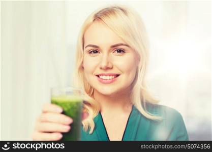 healthy eating, vegetarian food, diet, detox and people concept - smiling young woman drinking green vegetable juice or smoothie from glass at home. smiling woman drinking juice or smoothie at home