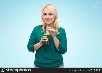 healthy eating, vegetarian food, diet, detox and people concept - smiling young woman drinking green vegetable juice or smoothie from glass over blue background