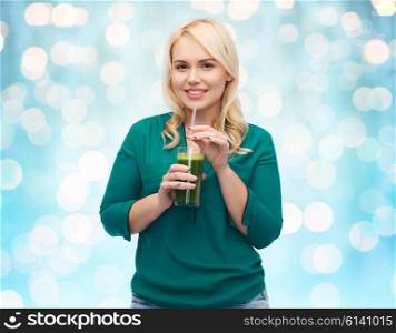 healthy eating, vegetarian food, diet, detox and people concept - smiling young woman drinking green vegetable juice or smoothie from glass over blue holidays lights background
