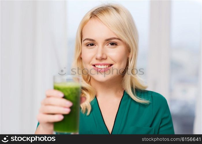 healthy eating, vegetarian food, diet, detox and people concept - smiling young woman drinking green vegetable juice or smoothie from glass at home