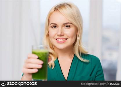 healthy eating, vegetarian food, diet, detox and people concept - smiling young woman drinking green vegetable juice or smoothie from glass at home