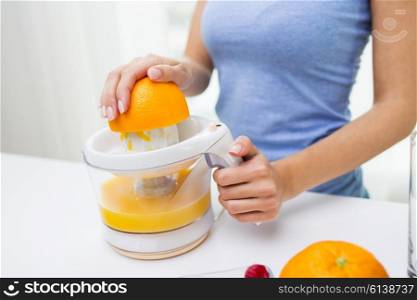 healthy eating, vegetarian food, dieting and people concept - close up of woman with squeezer squeezing orange juice at home