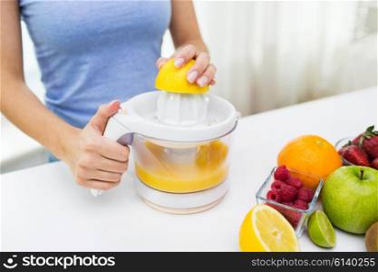healthy eating, vegetarian food, dieting and people concept - close up of woman with squeezer squeezing fruit juice at home