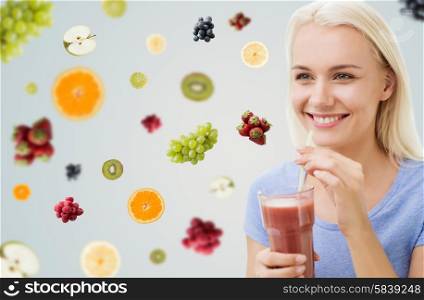healthy eating, vegetarian food, dieting and people concept - smiling woman drinking juice or shake from glass over fruits and berries on gray background