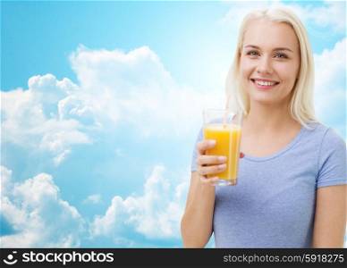 healthy eating, vegetarian food, dieting and people concept - smiling woman drinking orange juice or shake from glass over blue sky and clouds background