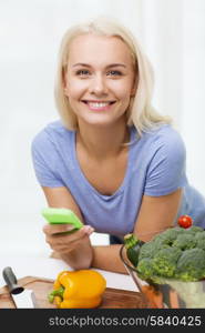 healthy eating, vegetarian food, dieting and people concept - smiling young woman with smartphone cooking vegetables at home