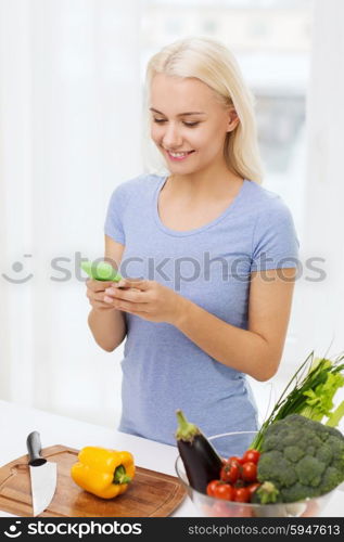 healthy eating, vegetarian food, dieting and people concept - smiling young woman with smartphone cooking vegetables at home