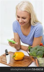 healthy eating, vegetarian food, dieting and people concept - smiling young woman with smartphone cooking vegetables at home