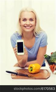 healthy eating, vegetarian food, dieting and people concept - smiling young woman cooking vegetables and showing blank smartphone screen at home