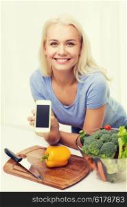 healthy eating, vegetarian food, dieting and people concept - smiling young woman cooking vegetables and showing blank smartphone screen at home