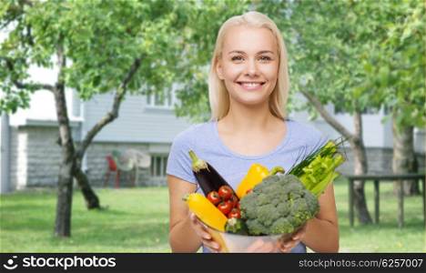healthy eating, vegetarian food, dieting and people concept - smiling young woman with bowl of vegetables over house and summer garden background