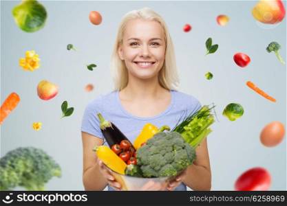healthy eating, vegetarian food, dieting and people concept - smiling young woman with bowl of vegetables over gray background with falling vegetables