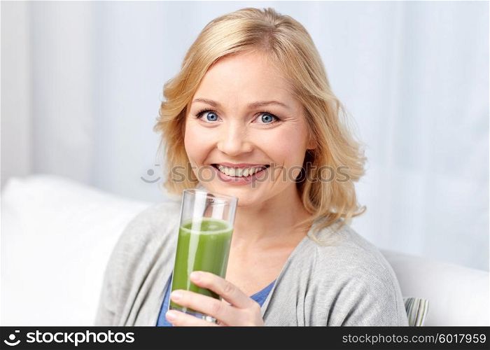 healthy eating, vegetarian food, dieting, detox and people concept - smiling middle aged woman drinking green fresh vegetable juice or smoothie from glass at home