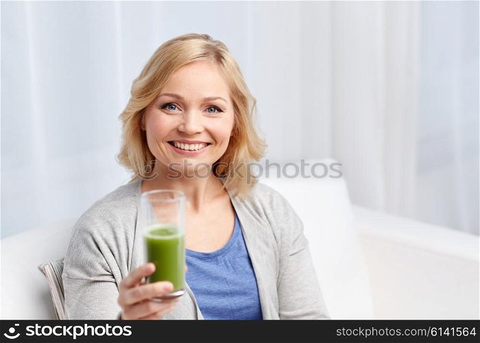 healthy eating, vegetarian food, dieting, detox and people concept - smiling middle aged woman drinking green fresh vegetable juice or smoothie from glass at home