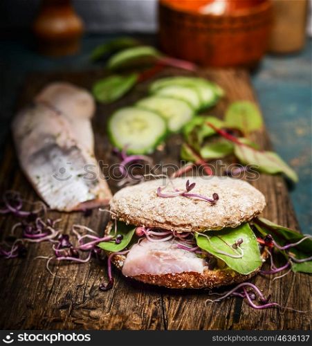 Healthy fish sandwich with herring, cucumber and sprouts on rustic kitchen table, side view
