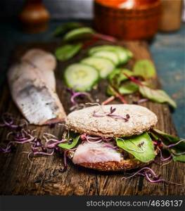 Healthy fish sandwich with herring, cucumber and sprouts on rustic kitchen table, side view