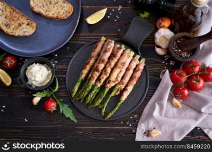 Healthy food - Asparagus wrapped with bacon and spices on a plate on wooden table.. Healthy food - Asparagus wrapped with bacon and spices on a plate on wooden table